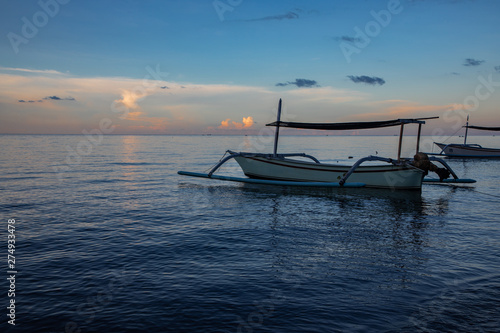 Blue hour over calm ocean and black sand beach with balinese boat