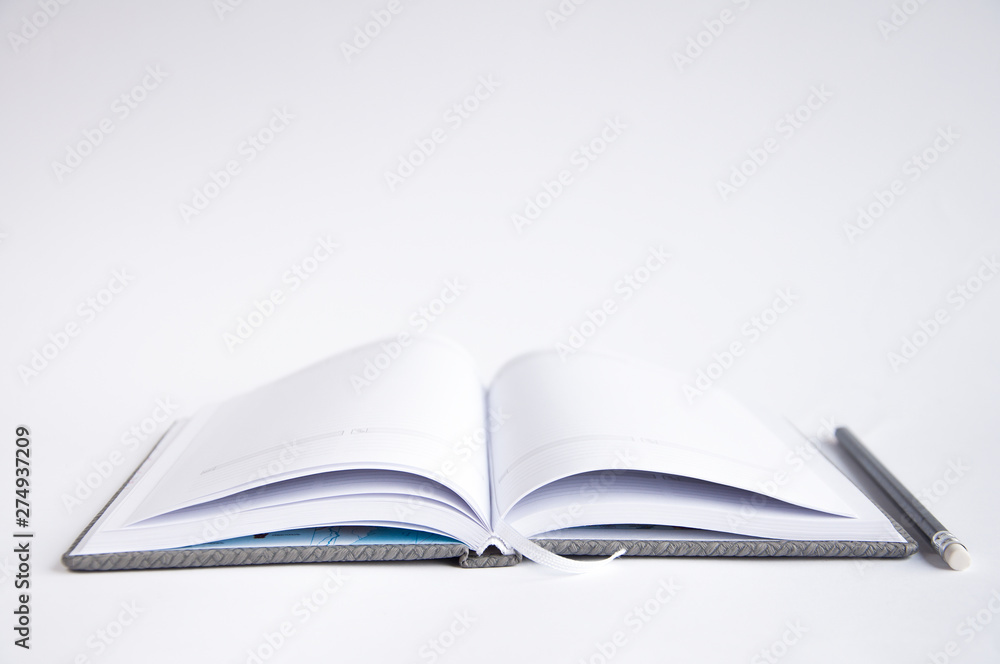 open notebook on the table. On the notebook is a black pencil. On a white background open notebook on the table. On the notebook is a black pencil. On a white background