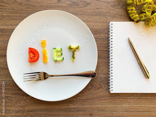 Word DIET made of sliced vegetables in white plate and diet plan on wood background