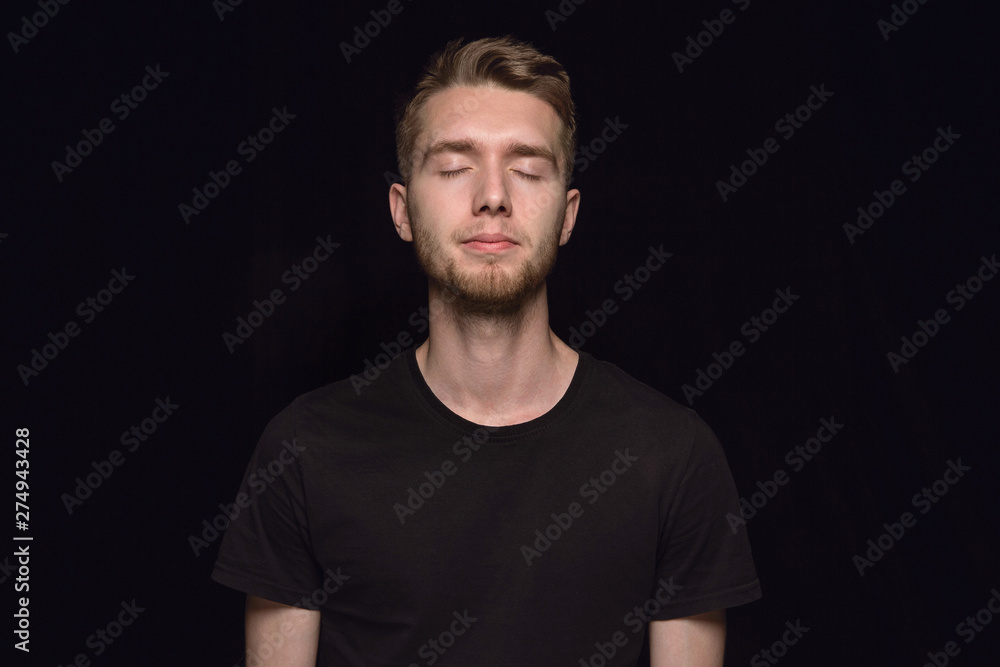 Obraz premium Close up portrait of young man isolated on black studio background. Photoshot of real emotions of male model with closed eyes. Thoughtful. Facial expression, human nature and emotions concept.