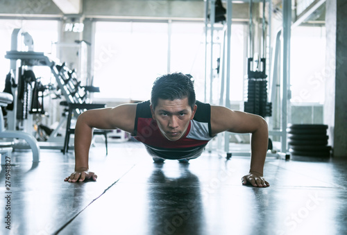 Sport. Young asian athletic man doing push-up muscular exercising in fitness gym.
