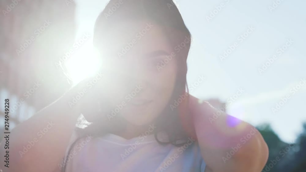 Close up view of beautiful brunette woman playfully posing on camera, seductively smiling and stroking her hair, blinks with her eye outdoors in sunlight. Sun lens, facial expression Close up view of beautiful brunette woman playfully posing on camera, seductively smiling and stroking her hair, blinks with her eye outdoors in sunlight. Sun lens, facial expression