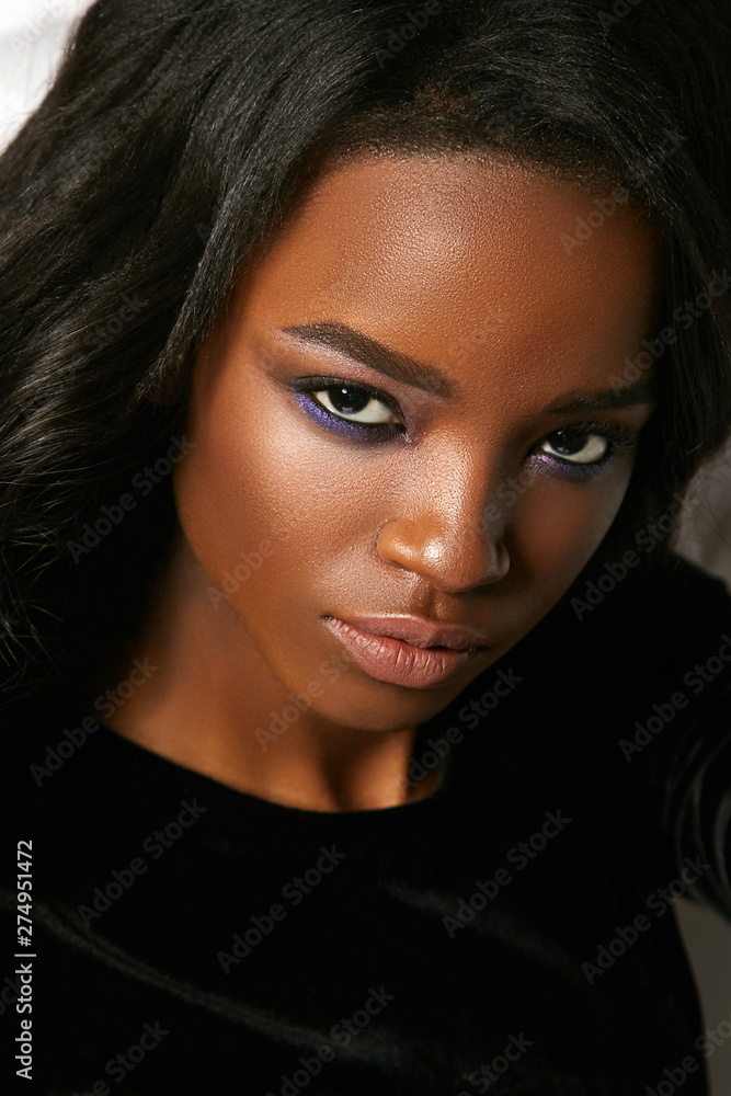 Fototapeta premium Beautiful young black girl seductively looking straight. Portrait of a girl in the studio in a velvet dress.