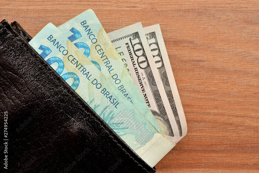 Obraz premium Carteira com notas de 100 reais e 100 dólares para investimento