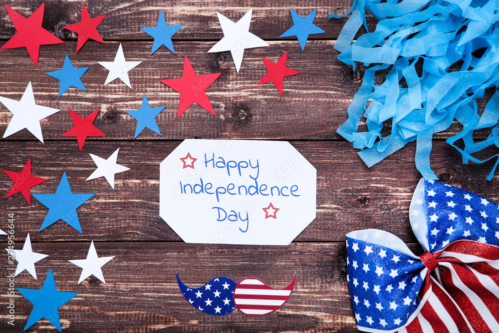 Fototapeta premium Text Happy Independence Day with paper stars and bow on brown wooden table