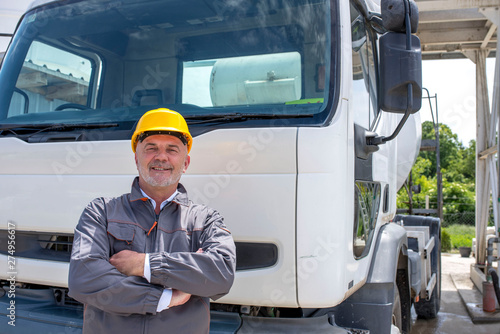 Smiling senior man, concrete truck driver, with safety helmet standing in front of the truck