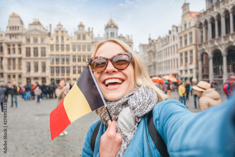 Woman tourist stands with the flag of Belgium on the background of the Grand-Place or the Grand Market Square in Brussels