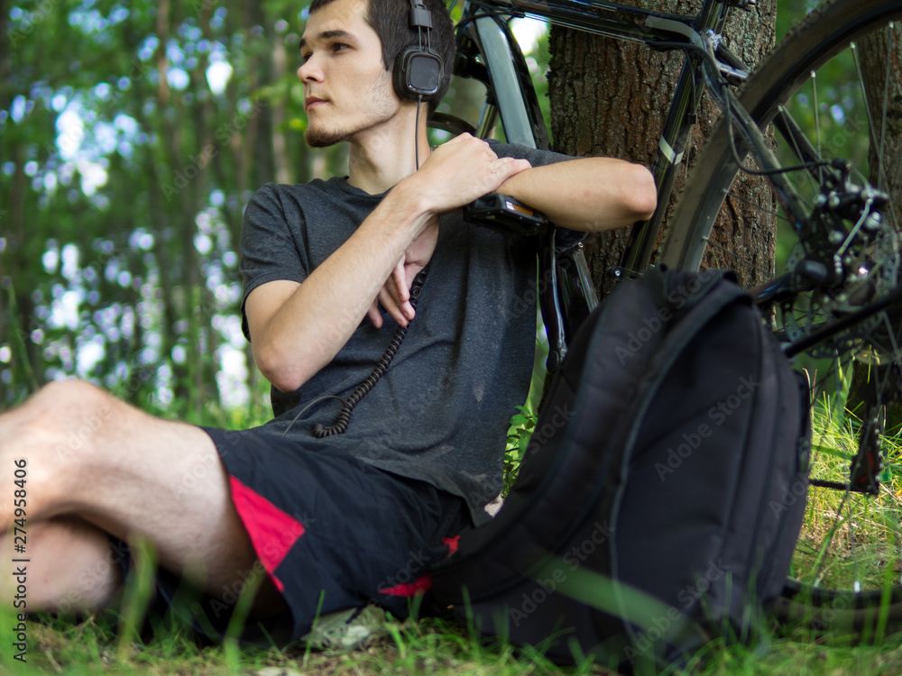Man cyclist resting in the Park by a tree and listening to music. Cycling in the forest Man cyclist resting in the Park by a tree and listening to music. Cycling in the forest
