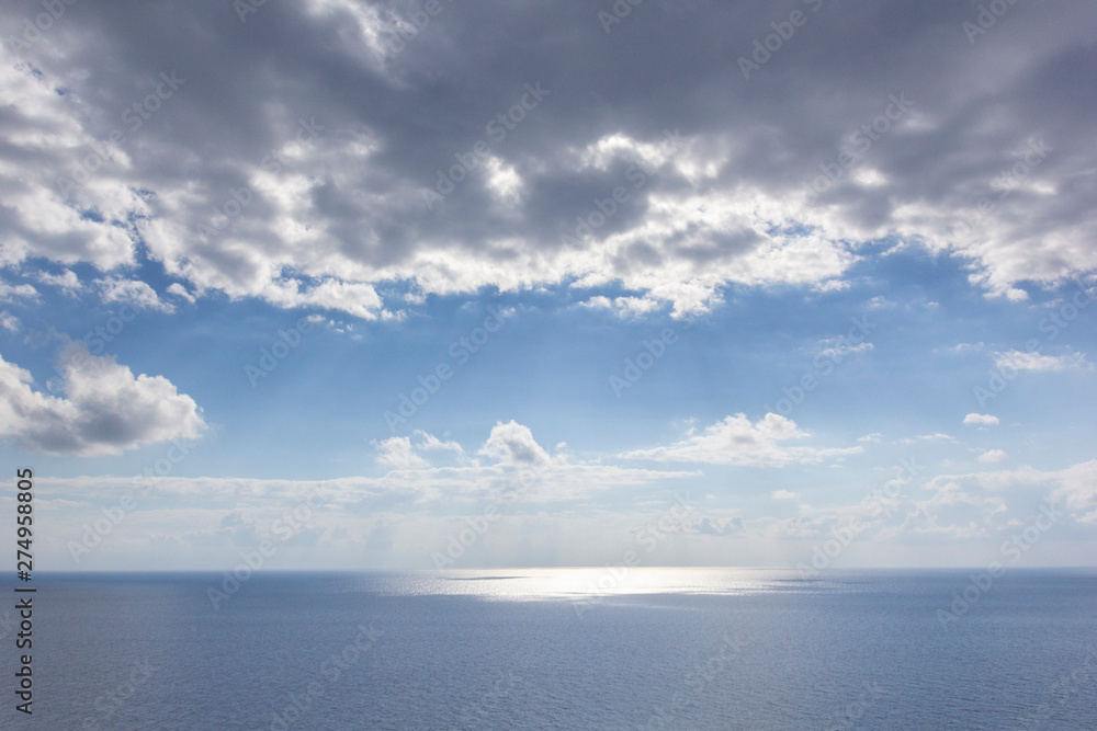 Background image of sky with clouds, sea, reflection of light on water, sun behind clouds