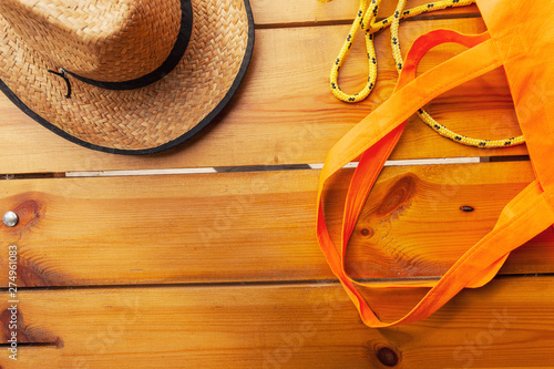 A wicker hat, a yellow rope, and an orange tote bag are laying on a wooden surface
