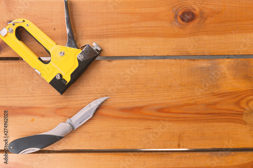 An automatic staple gun and a pocket knife are laying on a wooden surface