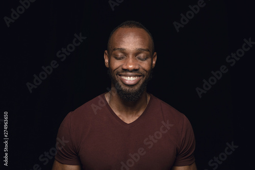 Close up portrait of young man isolated on black studio background. Photoshot of real emotions of male model with closed eyes. Thinking and smiling. Facial expression, human emotions concept.
