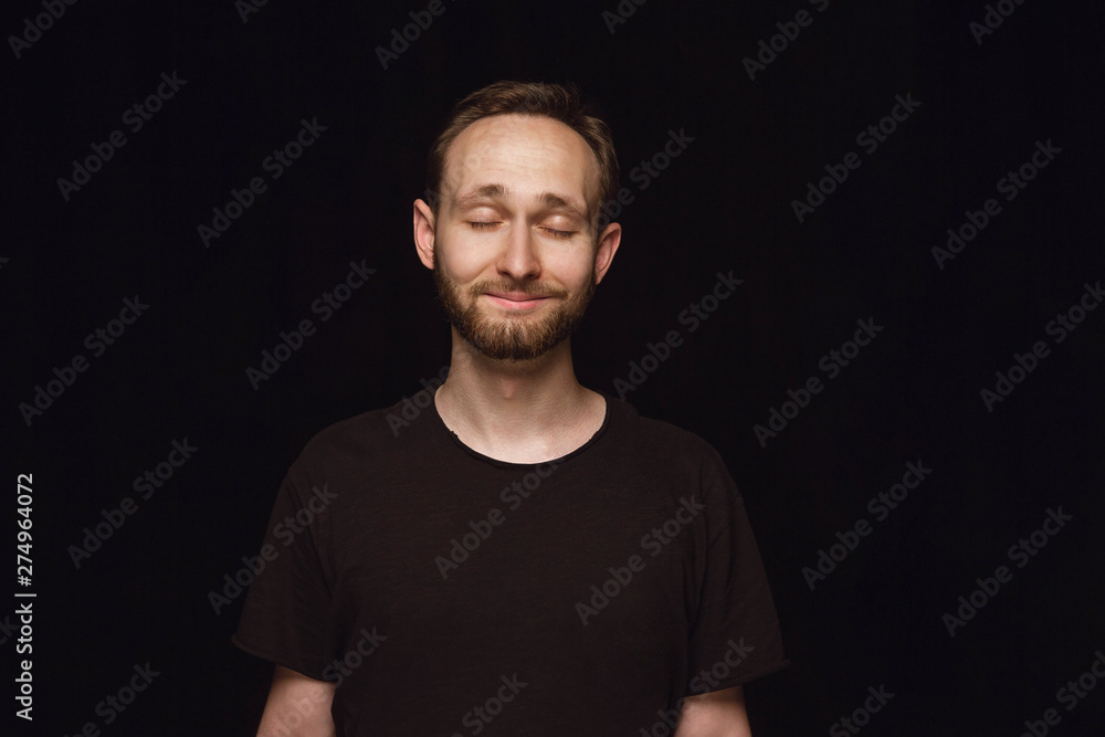 Close up portrait of young man isolated on black studio background. Photoshot of real emotions of male model with closed eyes. Thinking and smiling. Facial expression, human emotions concept. Close up portrait of young man isolated on black studio background. Photoshot of real emotions of male model with closed eyes. Thinking and smiling. Facial expression, human emotions concept.