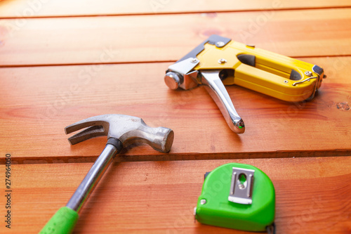 A hammer, measuring tape, and a staple gun are laying on a wooden surface