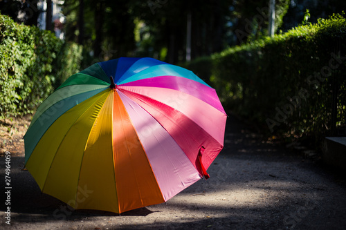 Umbrella with rainbow colors placed in the sun on a sidewalk in the park – Multicolored waterproof equipment used on rainy days © madrolly