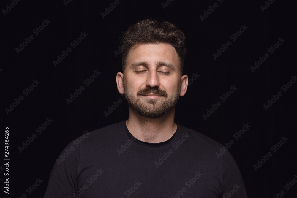 Close up portrait of young man isolated on black studio background. Photoshot of real emotions of male model with closed eyes. Thinking and smiling. Facial expression, human emotions concept. Close up portrait of young man isolated on black studio background. Photoshot of real emotions of male model with closed eyes. Thinking and smiling. Facial expression, human emotions concept.