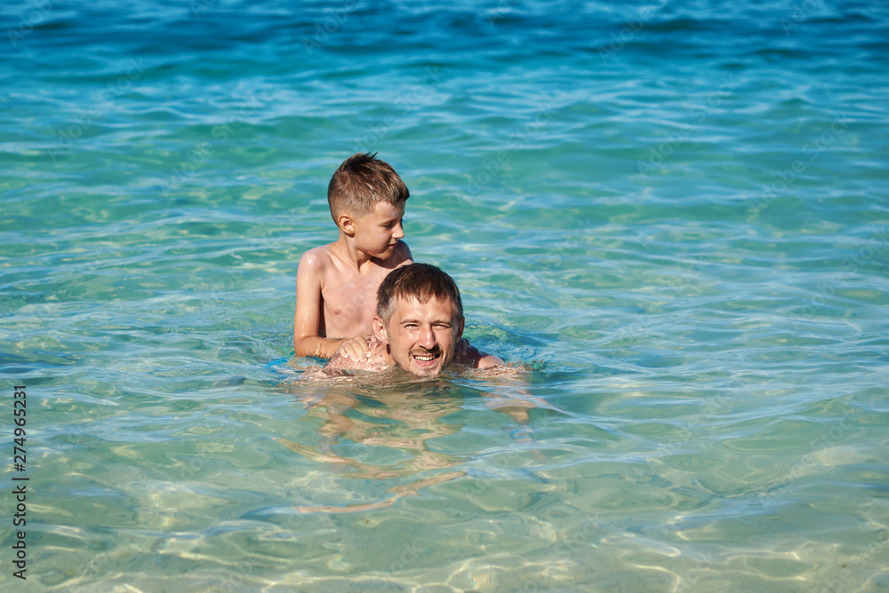 Active summer holidays. Father and son are swimming in the sea and enjoying their vacations..