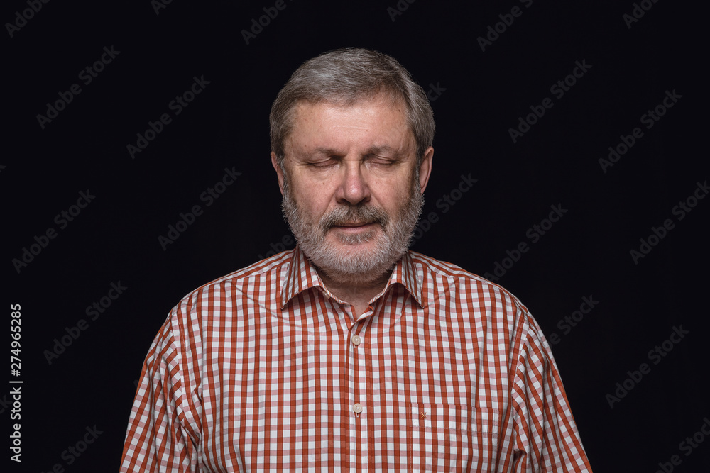 Obraz premium Close up portrait of senior man isolated on black studio background. Photoshot of real emotions of male model with closed eyes. Thinking and smiling. Facial expression, human emotions concept.
