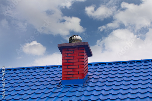 A red chimney with with revolving cowl on a blue metal roof. photo