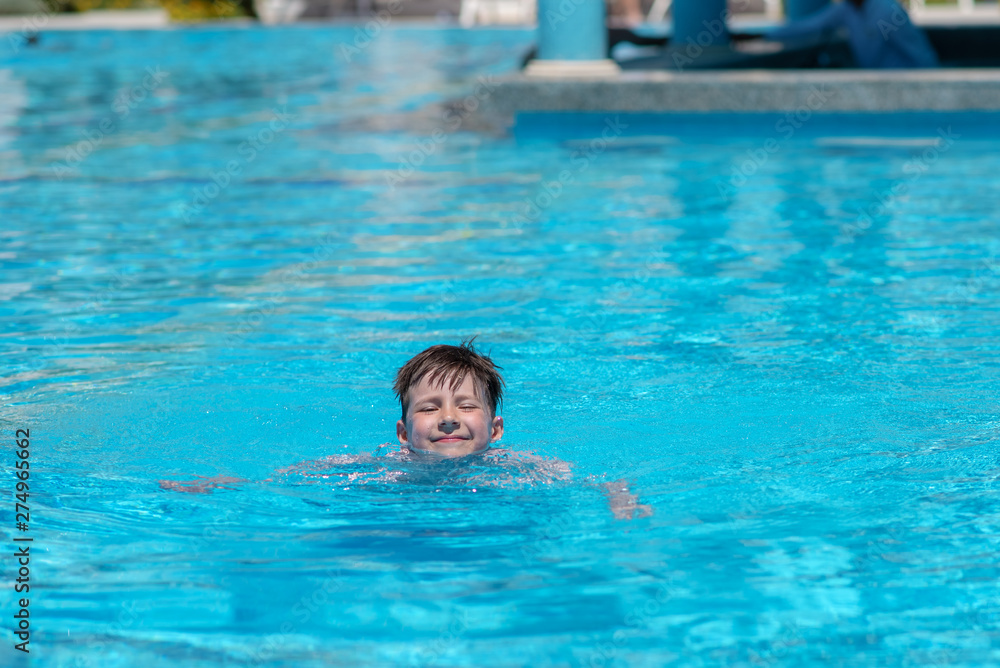 Portrait of smiling Caucasian boy spending time in pool at resort. He is enjoying his summer holidays.