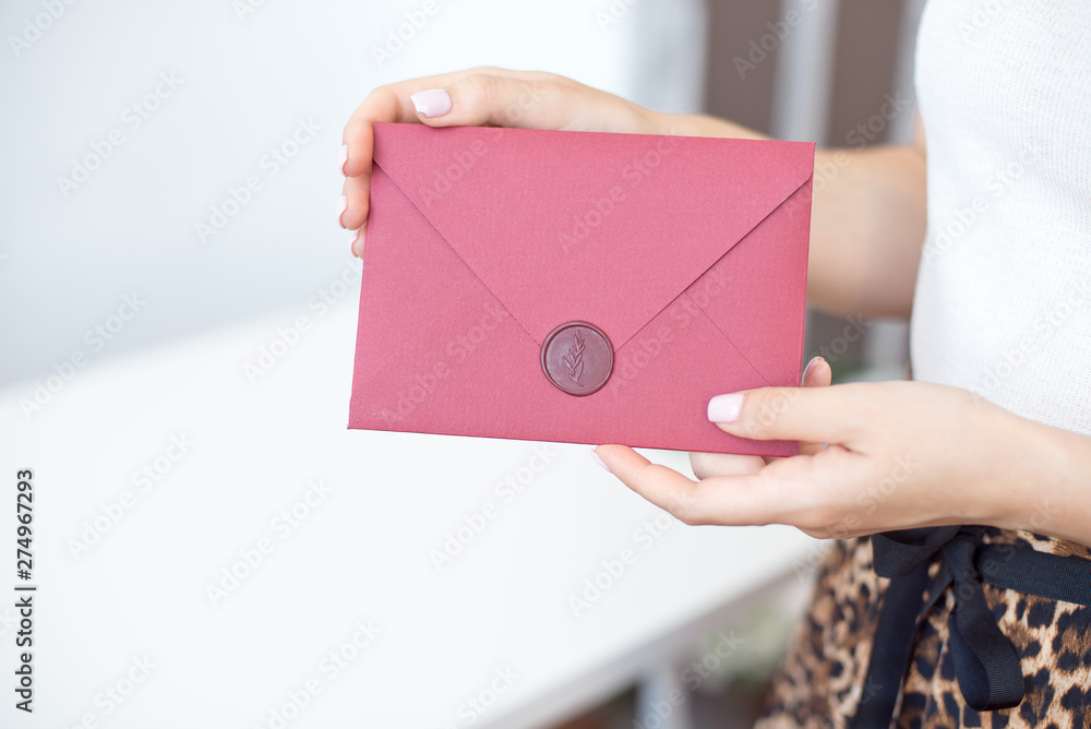 Close-up photo of female hands holding a silver invitation envelope with a wax seal, a gift certificate, a postcard, a wedding invitation card Close-up photo of female hands holding a silver invitation envelope with a wax seal, a gift certificate, a postcard, a wedding invitation card