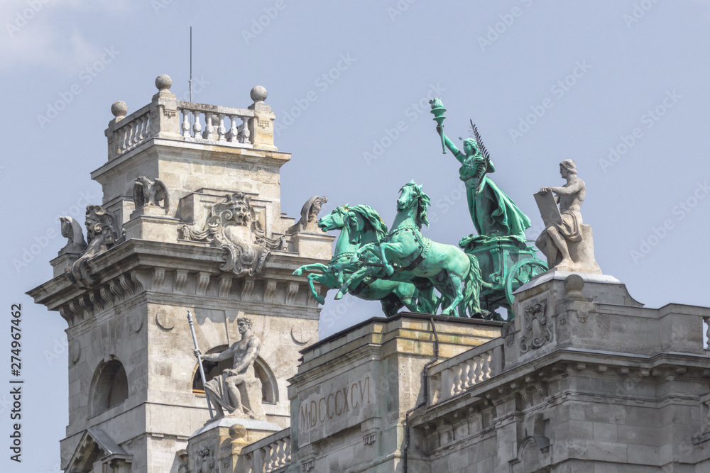 Obraz premium Parliament Building in Budapest. State institution in Hungary. Exterior of a historic building. Coats of arms on the wall. Statue with horses on the roof of the parliament. European architecture.