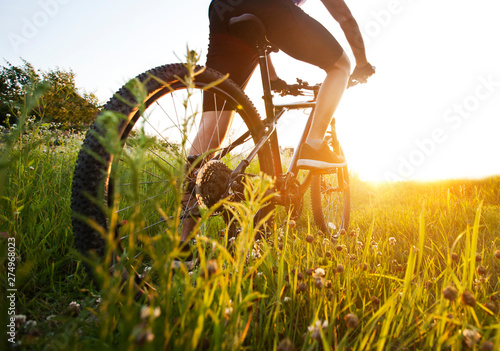 The young man is riding the bike through the path with a lot of grass and flowers  in the middle of the field