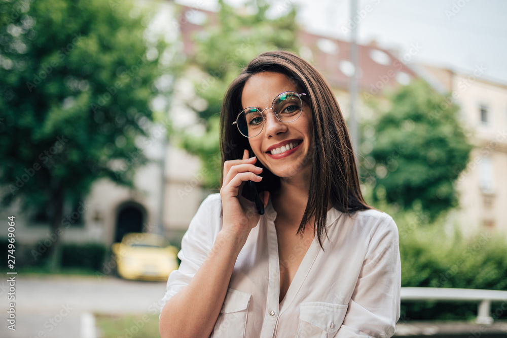 Portrait of beautiful smiling woman with eyeglasses using smart phone in the city, looking at camera. Portrait of beautiful smiling woman with eyeglasses using smart phone in the city, looking at camera.