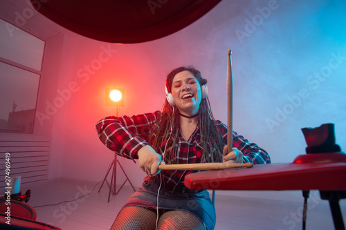 Electronic drum set, music and hobby concept - young woman drummer playing in headphones