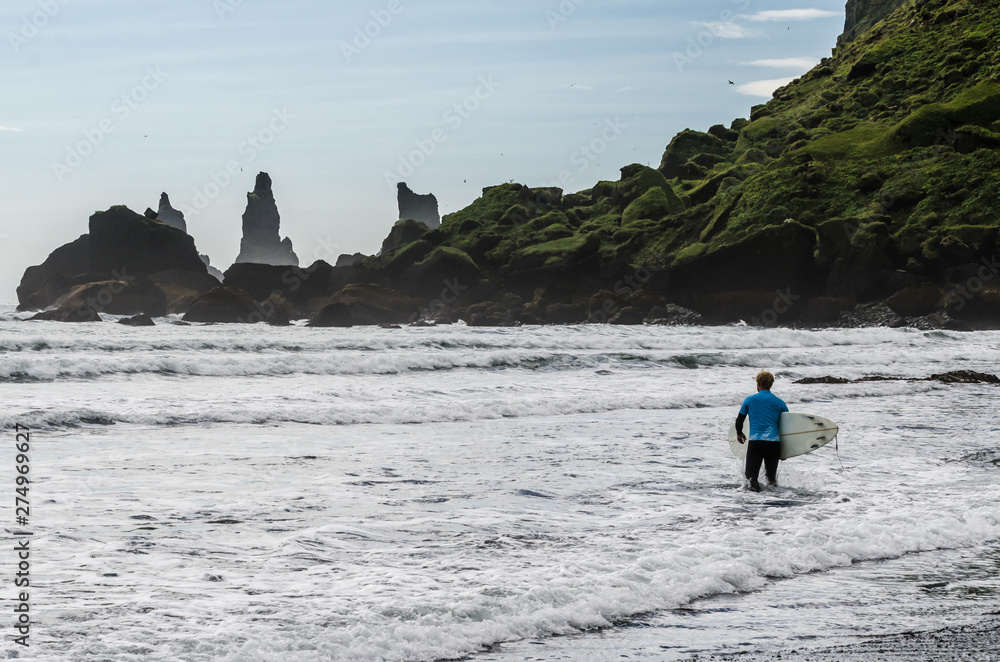 Surfer at the beach in Vic, Reynisfjara, Iceland, black beach, wild water, in front of the sea trolls in Iceland