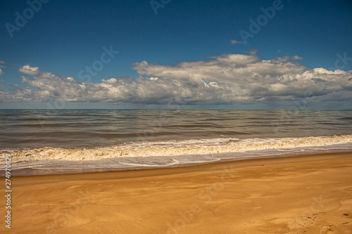 Calm sea on the coast. Small waves on the shore. Huge storm cloud over the sea. Free space.