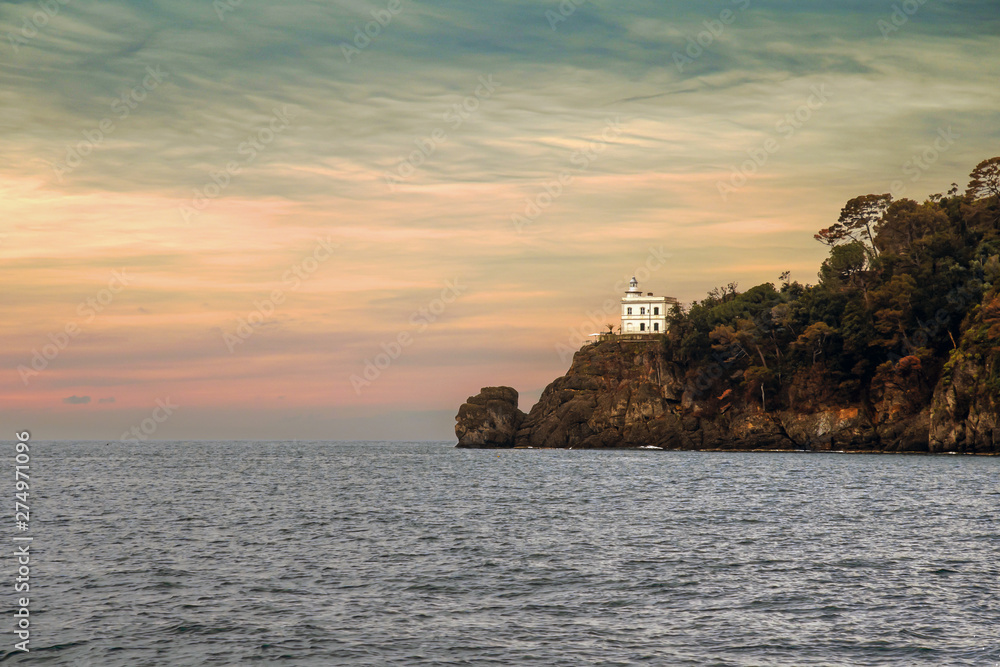 View of the tip of the promontory in the bay of Portofino, famous fishing village in the Levante Riviera, with the tower 12 meters high of the white lighthouse built in 1870, Genoa, Liguria, Italy