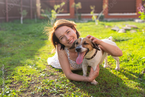 Positive cheerful woman playing with her beloved dog Jack Russell Terrier in the yard of her country house on a sunny summer day. Concept of love for animals and family recreation.
