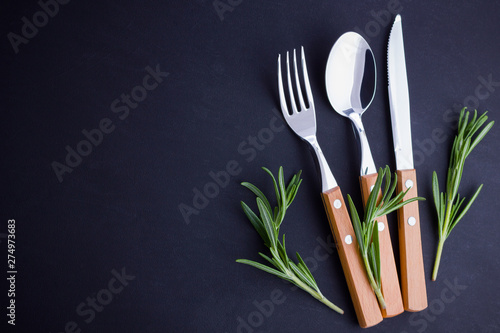Cutlery set. Knife, spoon, fork on dark background. Сutlery with rosemary. Black background. Table setting. Top view