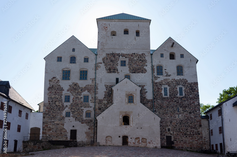 The brick towers of the inner facade and the paved authentic courtyard of the historic medieval castle-fortress Abo in Turku, Finland, on a sunny summer day.