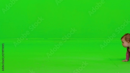 Cute baby girl crawling from side to side, stops in the middle, looks to the camera, smiles and continues, over a green screen.