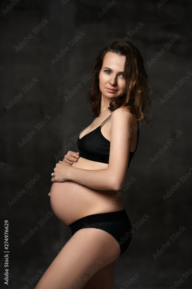 Beautiful young pregnant happy mother woman posing in underwear on dark Beautiful young pregnant happy mother woman posing in underwear on dark