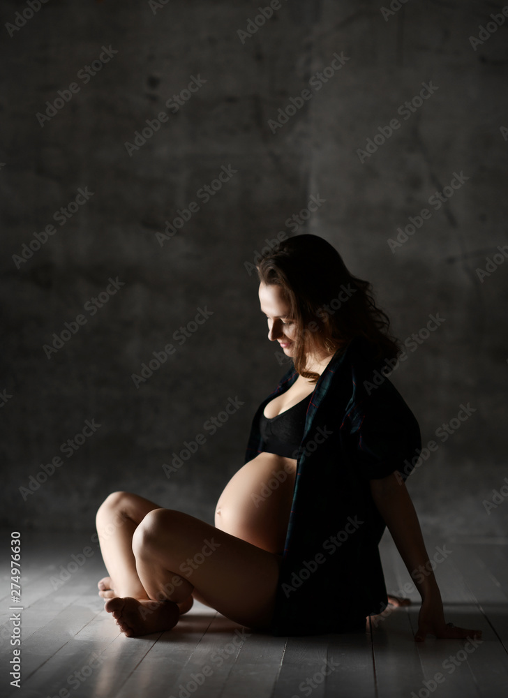 Naklejka premium Beautiful young pregnant happy mother woman posing in underwear on dark 