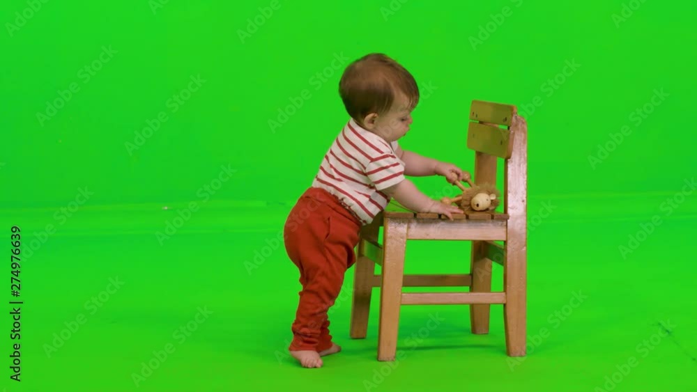 Playing happily while standing using a chair by a cute baby girl over a green screen. Playing happily while standing using a chair by a cute baby girl over a green screen.