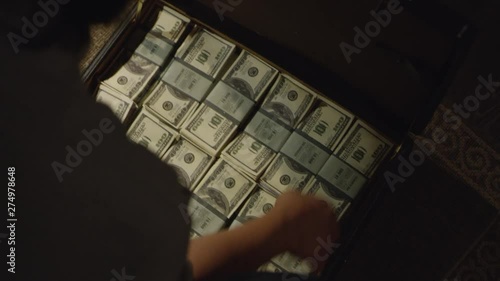 Young man counting bunches of US dollars from the suitcase in a room