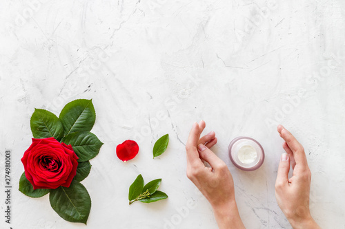 Natural floral cosmetics with rose flowers for face and body in hands care on white marble background top view mock up