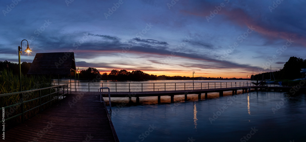 Piękny zachód słońca nad jeziorem Kalwa na Mazurach w Polsce., na pierwszym planie pomost na jeziorze.