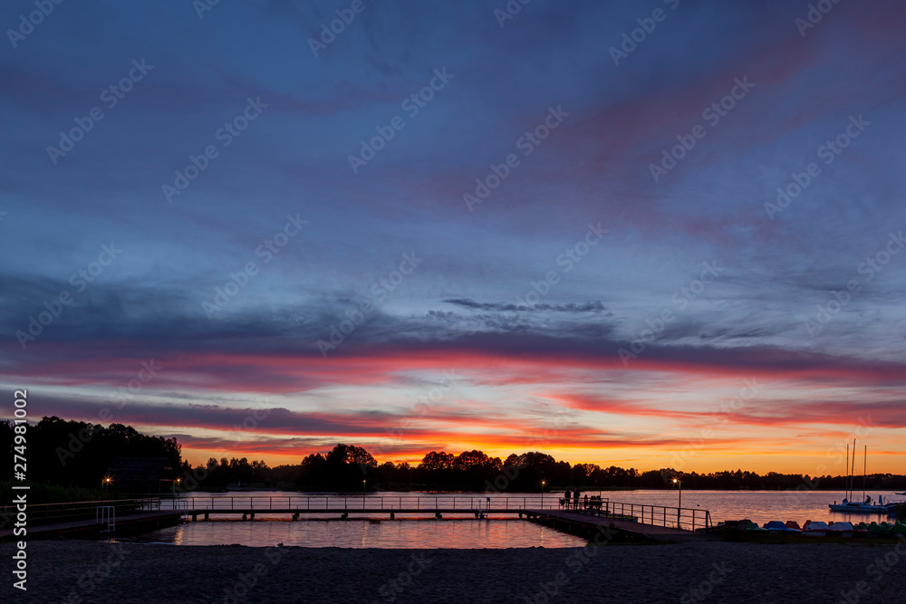 Piękny zachód słońca nad jeziorem Kalwa na Mazurach w Polsce., na pierwszym planie pomost na jeziorze.