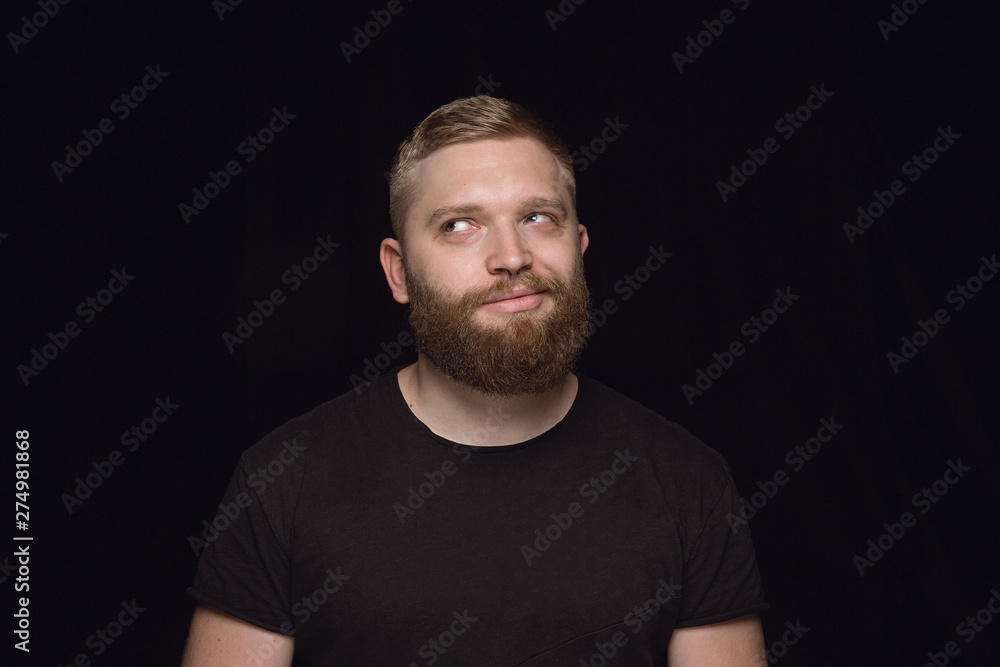 Close up portrait of young man isolated on black studio background. Photoshot of real emotions of male model. Dreaming and smiling, hopeful and happy. Facial expression, human emotions concept.