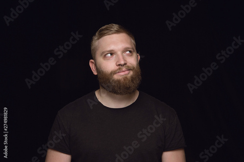 Close up portrait of young man isolated on black studio background. Photoshot of real emotions of male model. Dreaming and smiling, hopeful and happy. Facial expression, human emotions concept.