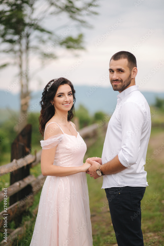 Lovestory of beautiful couple in the mountains, Handsome bearded man with beautiful and charming woman. Couple stand in front of beautiful tree Lovestory of beautiful couple in the mountains, Handsome bearded man with beautiful and charming woman. Couple stand in front of beautiful tree