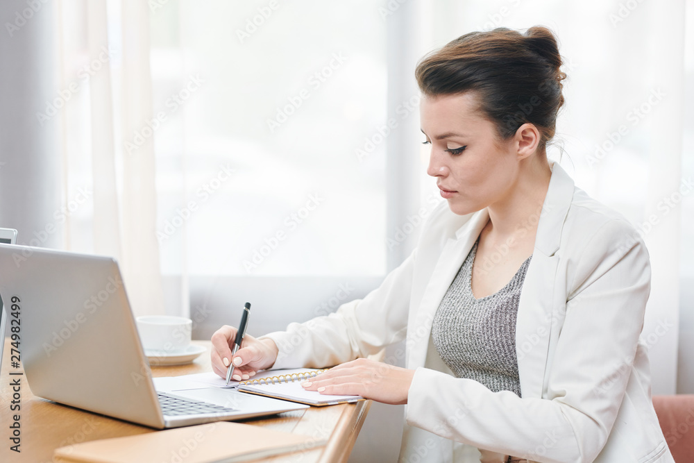 Serious concentrated businesswoman in white jacket sitting at table Serious concentrated businesswoman in white jacket sitting at table
