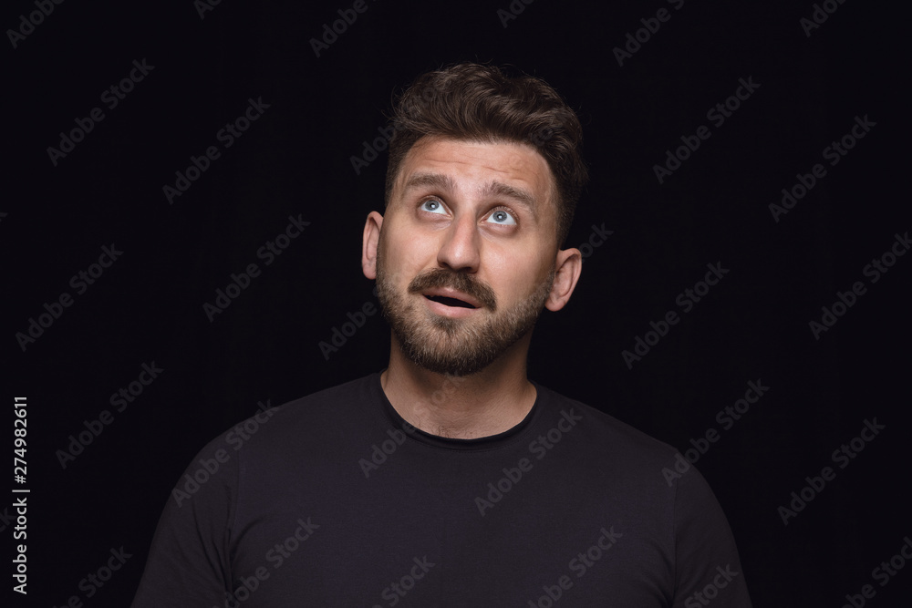 Close up portrait of young man isolated on black studio background. Photoshot of real emotions of male model. Dreaming and smiling, hopeful and happy. Facial expression, human emotions concept.