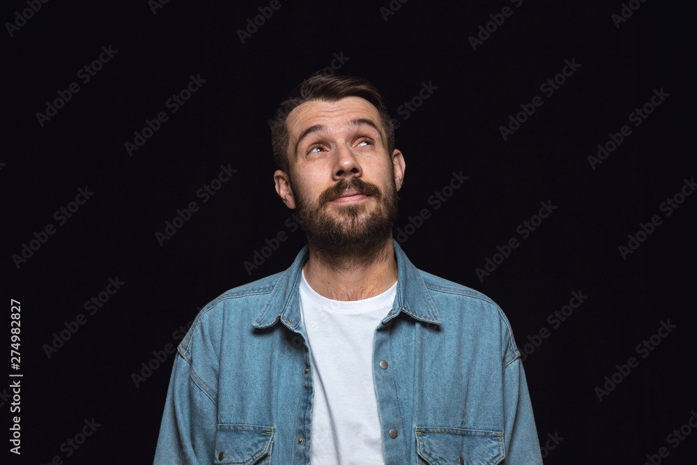 Close up portrait of young man isolated on black studio background. Photoshot of real emotions of male model. Dreaming and smiling, hopeful and happy. Facial expression, human emotions concept.