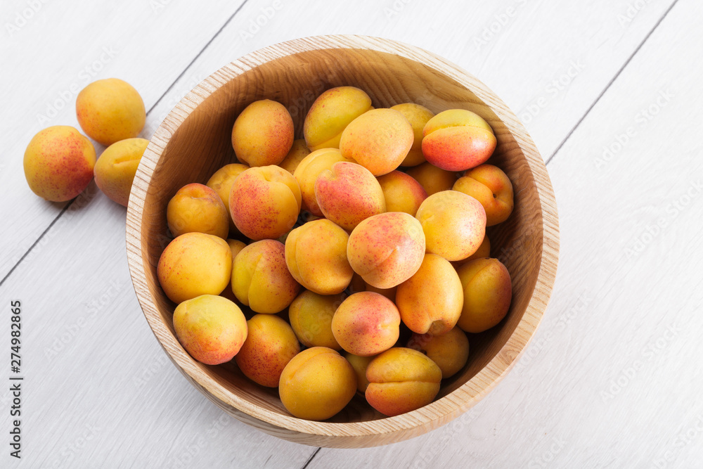 ripe organic apricots fruits in ash tree wooden bowl on a white wooden background